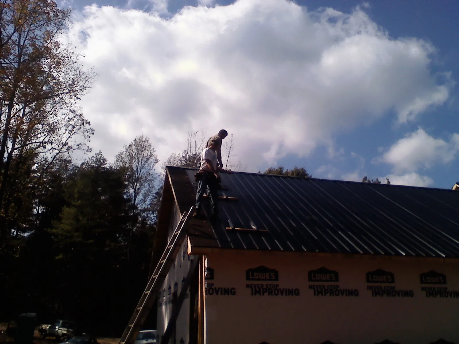 Roofer fastening dark metal panels high against a cloudy sky, from a Roof Inspection job in Spencer